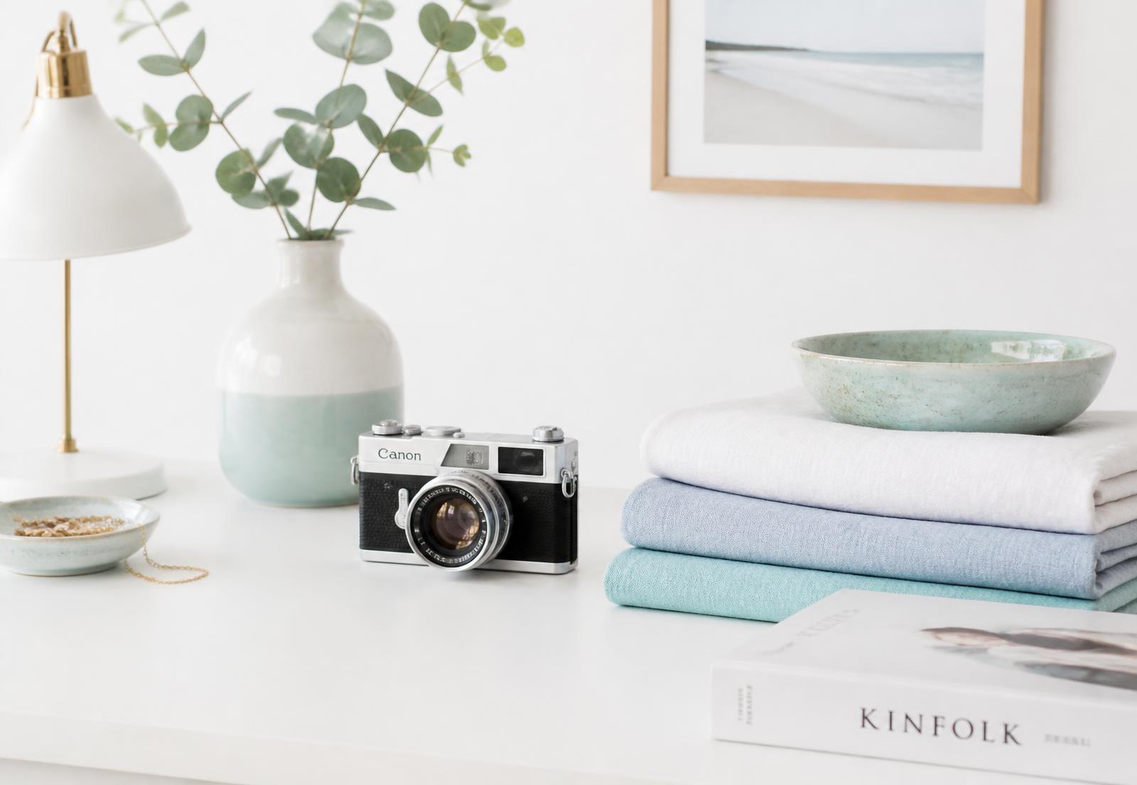Bright styled desk with a camera, ceramics and folded linens